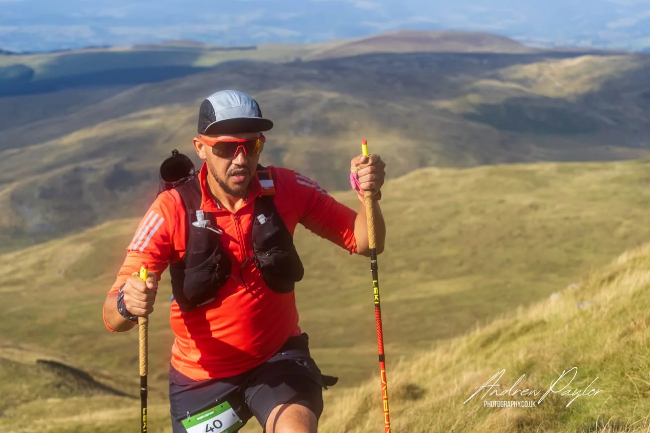 Daniel Dublin in a red top using running poles on a Welsh hillside, wearing race number 40