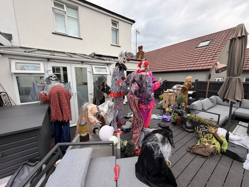 Clown and skeleton animatronics standing among garden furniture on a back deck
